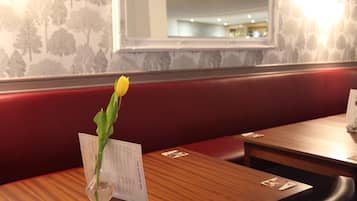 Ein Restaurantinneres mit einem Holztisch, einer Speisekarte und einer Vase mit einer einzelnen gelben Blume.