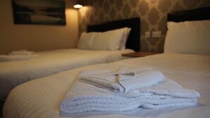 A hotel room with two beds, each with white linens and pillows. There is a stack of folded towels on the bed in the foreground. - Alcester Inn (Alcester)