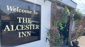 A sign welcoming visitors to The Alchemist Inn, featuring a brick facade and potted plants. - Alcester Inn (Alcester)