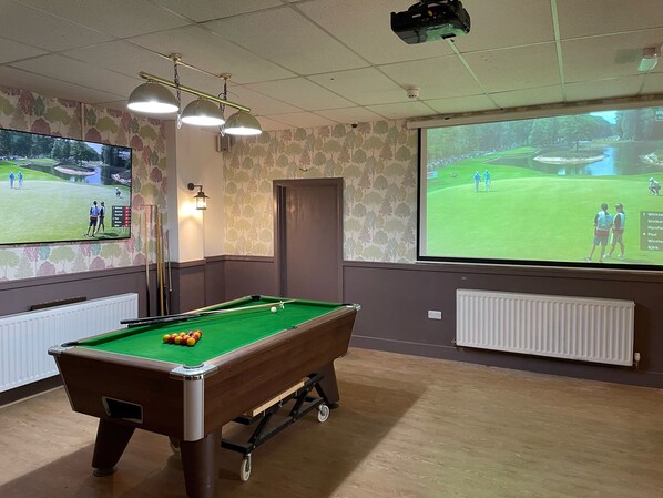 A pool table in a room with a large screen displaying a golf game.