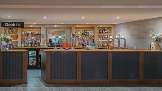 A check-in counter with a 'Check In' sign, a vending machine, and a display of various items. - Alcester Inn (Alcester)