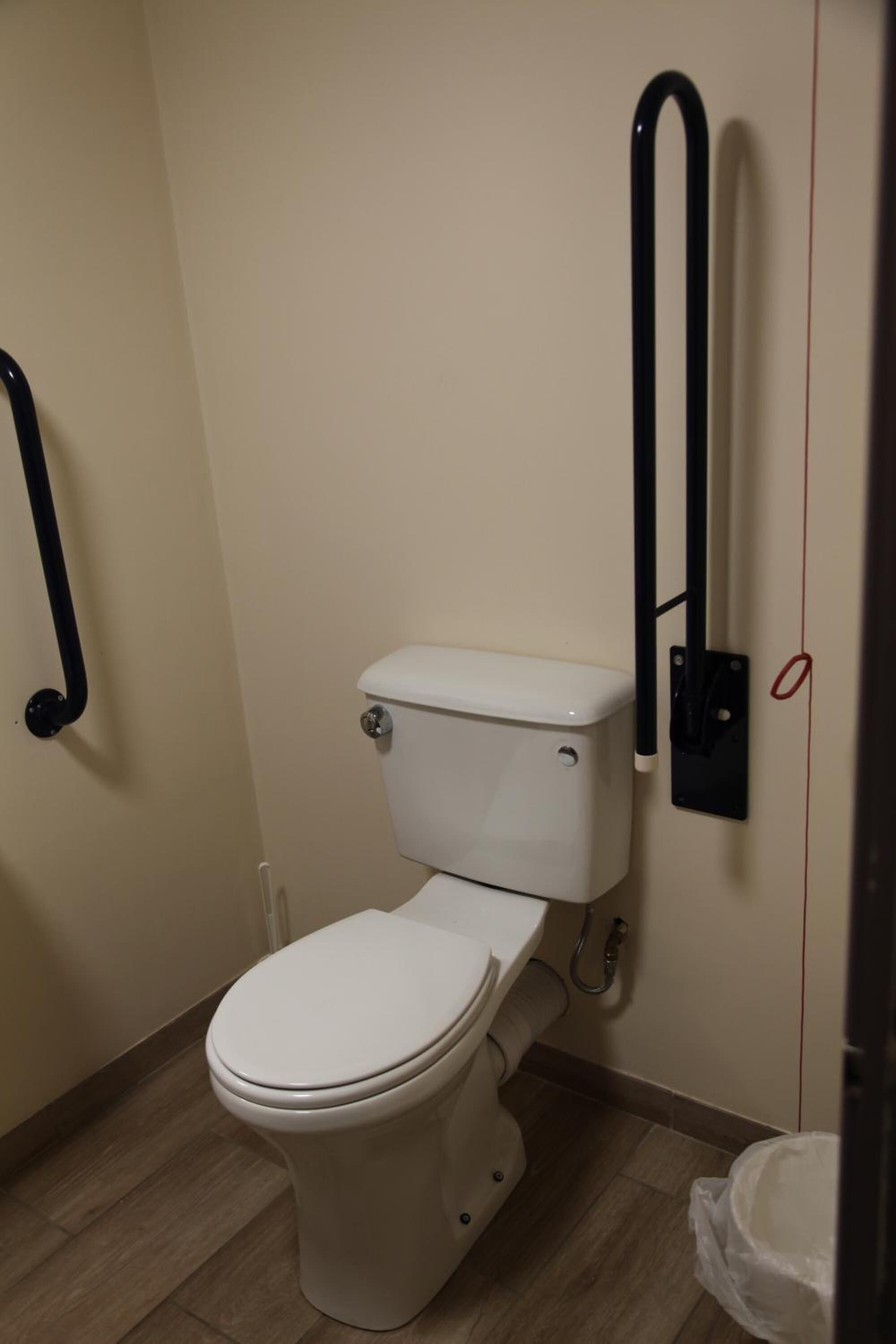 Baño pequeño y funcional con inodoro blanco, barra de apoyo negra y cesto de basura blanco.
