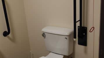 Baño pequeño y funcional con inodoro blanco, barra de apoyo negra y cesto de basura blanco.