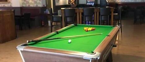 A pool table in a room with a bar area, chairs, and a ceiling with a light fixture.