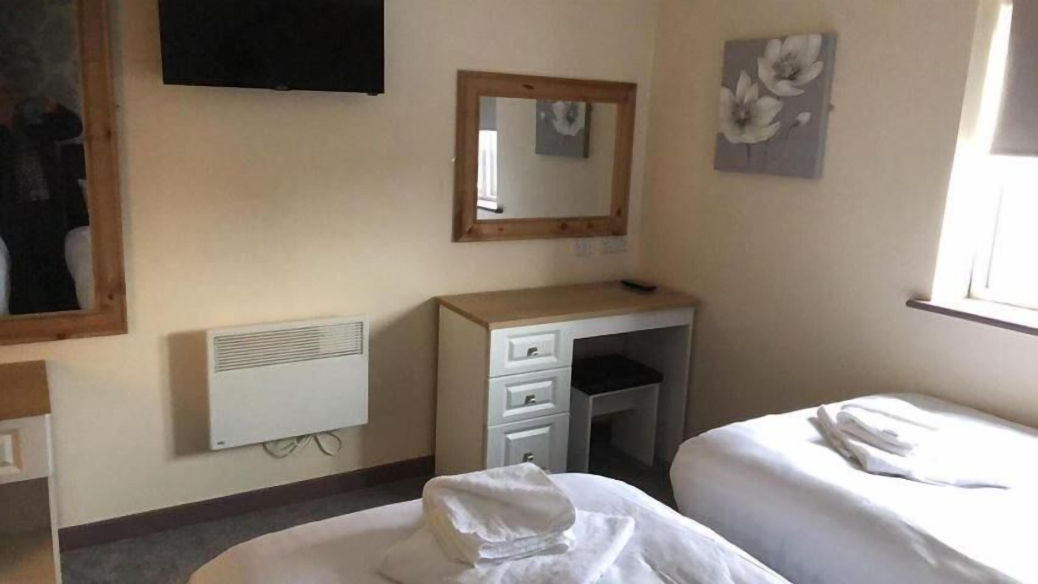 Une chambre d’hôtel avec un lit, un bureau avec des tiroirs, un miroir, un radiateur et une fenêtre.
