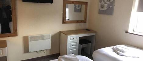 Une chambre d’hôtel avec un lit, un bureau avec des tiroirs, un miroir, un radiateur et une fenêtre.