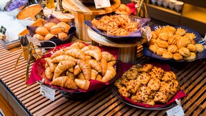 Un bufé con diversas opciones de panadería, incluyendo cruasanes y pasteles, dispuesto sobre mesas de madera.
