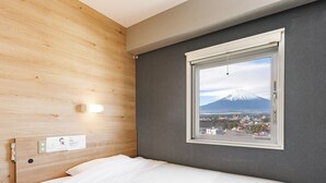 Habitación de hotel con cama, pared de madera, pared gris y ventana con vistas a una montaña.