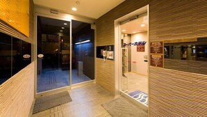 Entrada de hotel con puerta de cristal, pared de madera y suelo de baldosas.