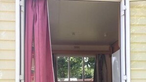 A compact room with a kitchenette, a dining table, and a window with curtains. - Camping de Lagraulière (Perpezac-le-Noir)