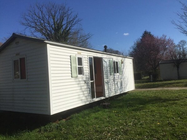 A single-story mobile home with a front door, two windows, and a chimney.