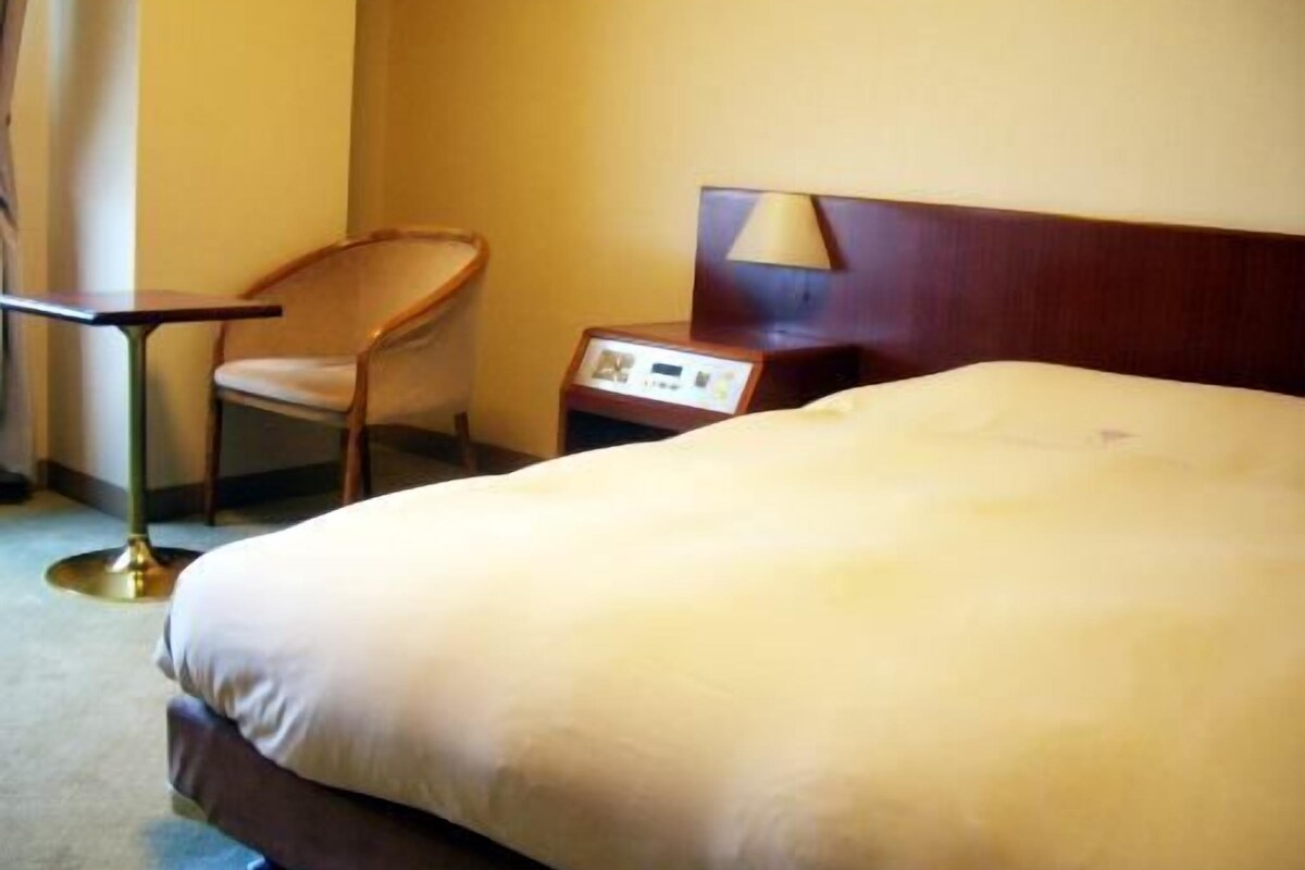 Een hotelkamer met een bed, een stoel, een nachtkastje en een lamp.