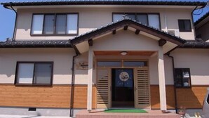 A two-story house with a wooden facade, a tiled roof, and a green mat at the entrance. - Minshuku Kazu (Kami)