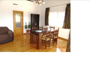 Cozy living space with a dining table and comfortable seating for six, a sofa, and a large window with a potted plant.