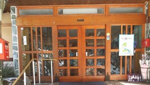 A building with a wooden facade, a set of stone steps leading to a door with glass panels, and a sign with Japanese text.