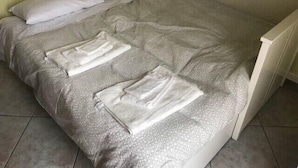 A bed with a patterned grey bedspread and two neatly folded white towels.