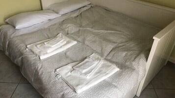 Un lit recouvert d’une couverture grise à motifs et agrémenté de deux serviettes blanches soigneusement pliées.