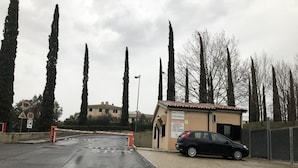 A gated parking area with a black car parked inside, a small building with a sign, and tall trees in the background.
