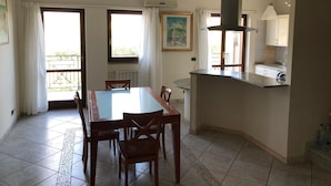 A dining area with a large table and chairs, a kitchen with a sink and stove, and a balcony with a railing.