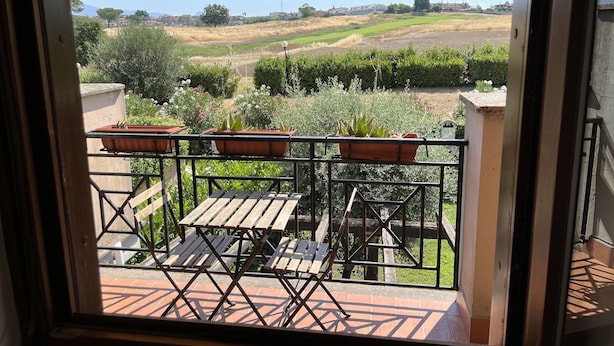 A balcony with a red and yellow striped awning, wooden tables and chairs, and potted plants.