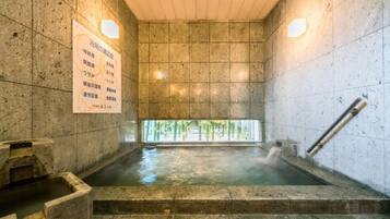 Een natuurstenen bad met warm water, een houten plafond en een bord waarop voorzieningen staan.