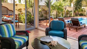 Une terrasse ensoleillée, meublée de mobilier en osier, avec une piscine et des plantes tropicales.
