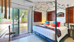 Une chambre à coucher comprenant un lit, un ventilateur de plafond, une fenêtre avec des rideaux et une porte donnant sur un balcon.