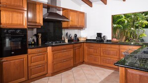 Une cuisine avec des meubles de rangement en bois, un poêle noir et une fenêtre donnant sur un paysage verdoyant.