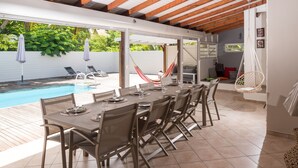 Un espace extérieur aménagé pour les repas, avec une piscine, un plafond en bois et un hamac.