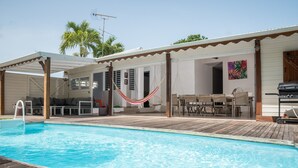 Un espace piscine doté d’une terrasse en bois, d’un hamac, de meubles de jardin et d’un barbecue.