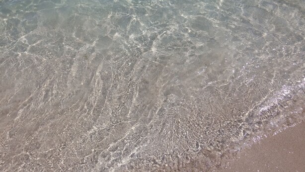 Primer plano de una playa con agua cristalina y arena visible.