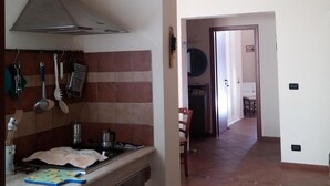 Cocina con estufa, horno y utensilios colgando. Hay una puerta que da a otra habitación.