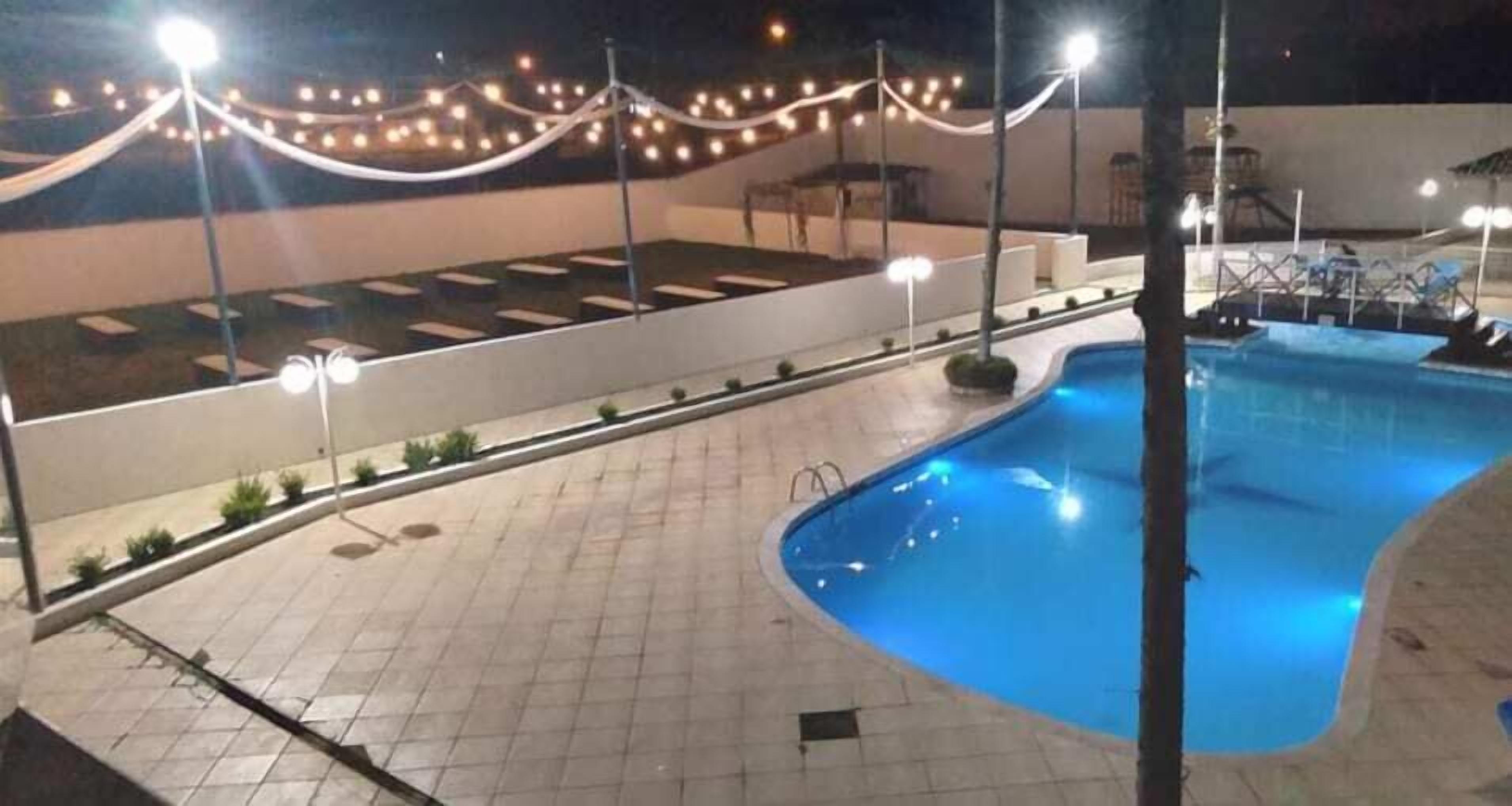 A swimming pool area with tiled flooring, a pool, and string lights.