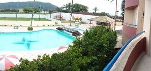 Una piscina con diseño en forma de estrella, rodeada por una valla, con un parque infantil y un pequeño pabellón al fondo.
