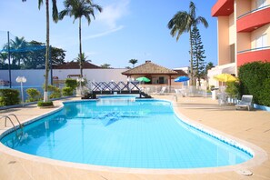 A swimming pool with a tiled edge, surrounded by palm trees and a building with a red facade.