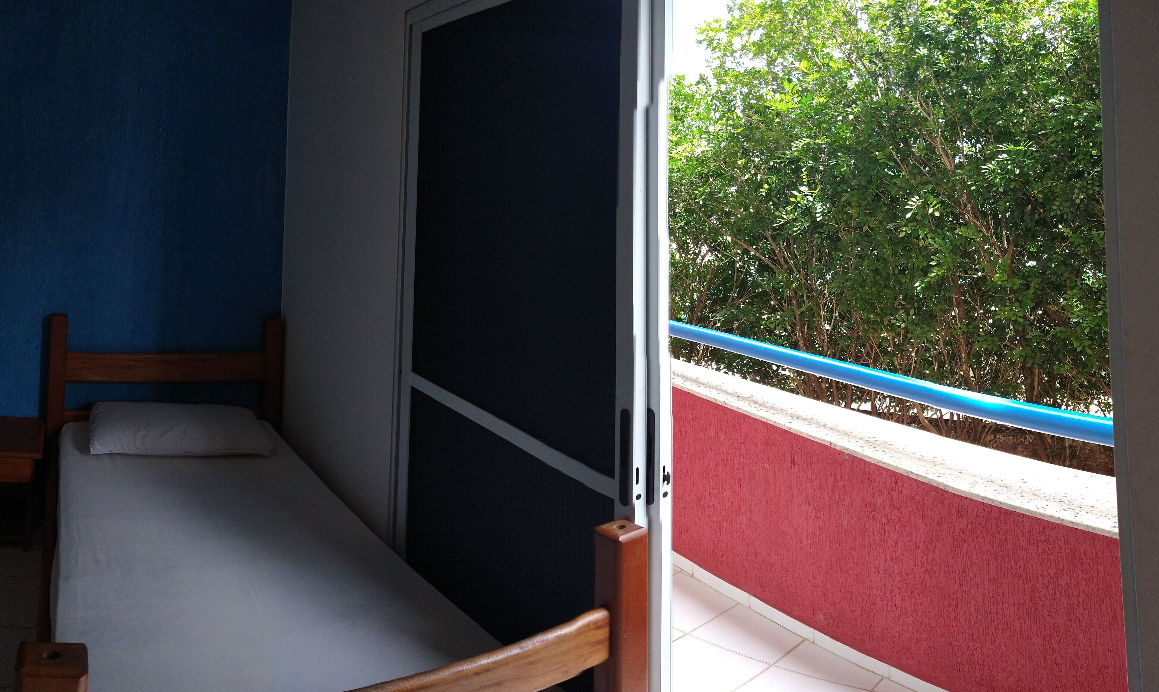 A room with a bed, a window, and a view of greenery outside.