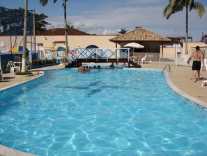 Una piscina con agua cristalina azul, rodeada de palmeras y una estructura de techo con azulejos.