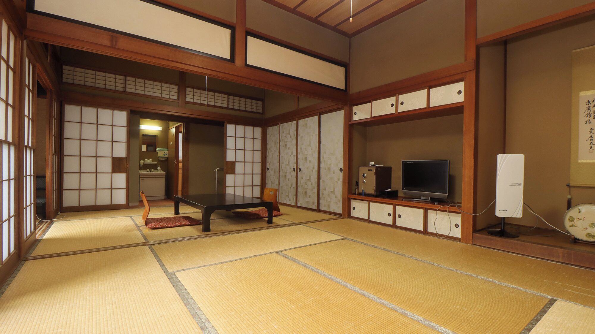 A traditional Japanese room with tatami flooring, a low table, sliding doors, and a TV on a cabinet.