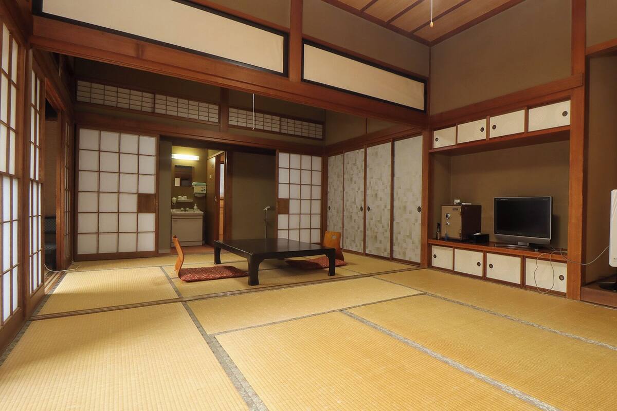 Een traditionele Japanse kamer met tatami vloeren, een lage tafel, schuifdeuren en een televisie op een kast.