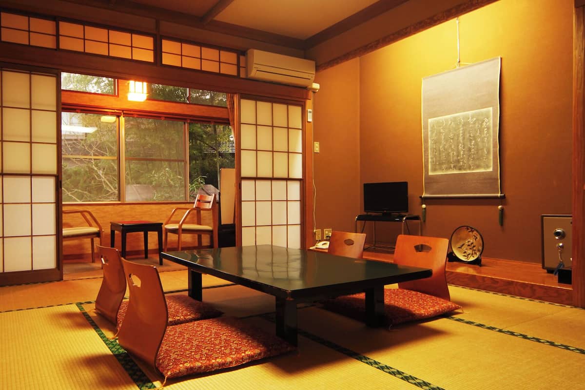 Een traditionele Japanse kamer met tatami vloerbedekking, een lage tafel, stoelen, een televisie en een schuifdeur met shoji schermen.