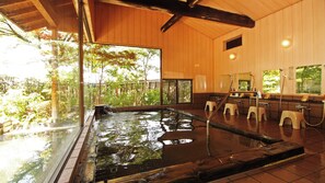 A traditional Japanese onsen with a wooden interior, a large window overlooking greenery, and a wooden deck leading to the hot spring. - Suehirokan (Tagami)
