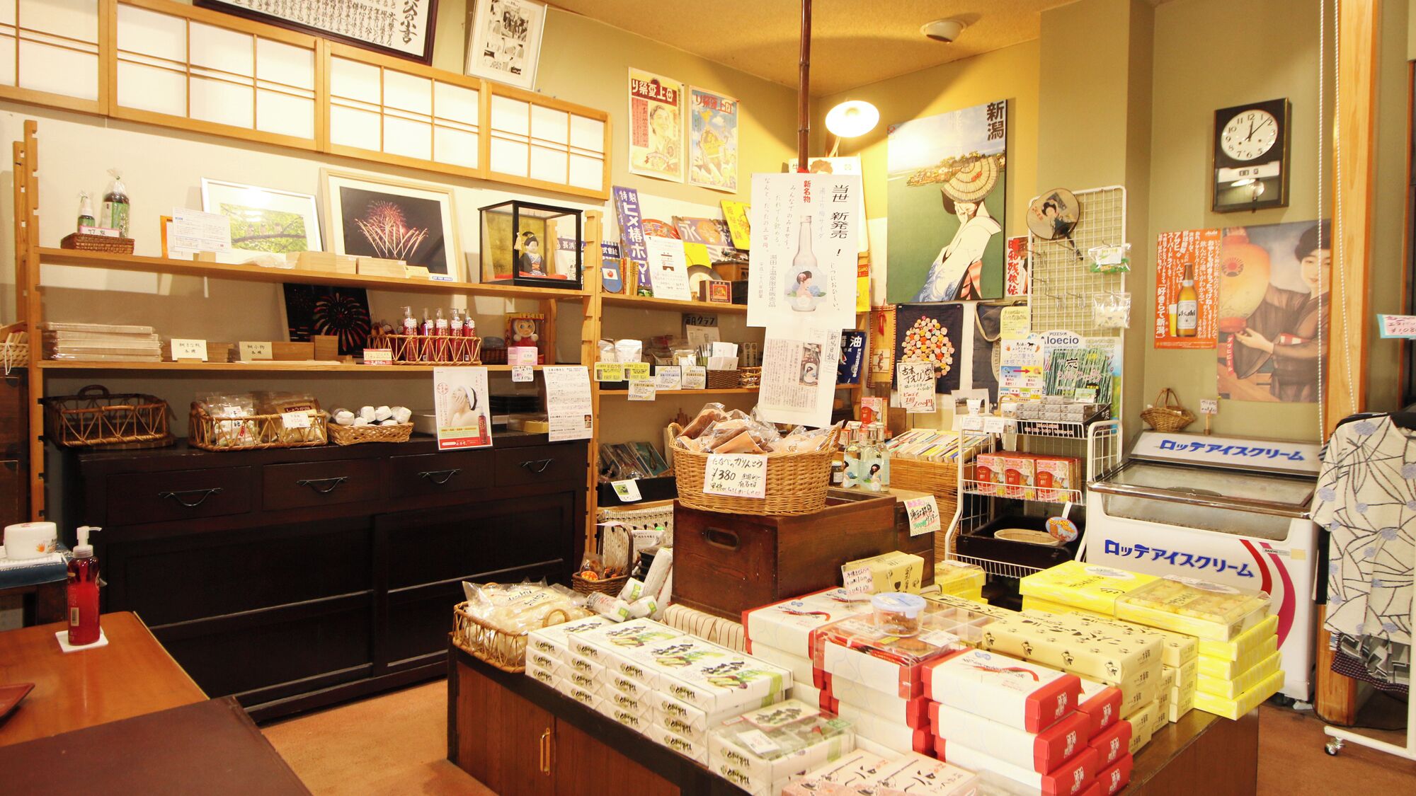 Un commerce japonais traditionnel, avec des étagères remplies de produits, un comptoir où sont exposés des articles emballés, ainsi que divers panneaux et affiches accrochés aux murs.