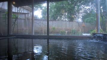A pool with a waterfall feature, surrounded by a wooden fence and trees.