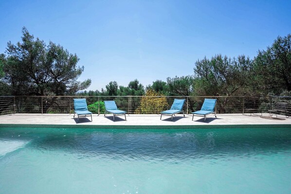 A swimming pool with four blue lounge chairs aligned along the edge. - Villa (Saint-Marc-Jaumegarde)