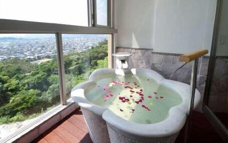 A bathtub with rose petals on a balcony with a city view.