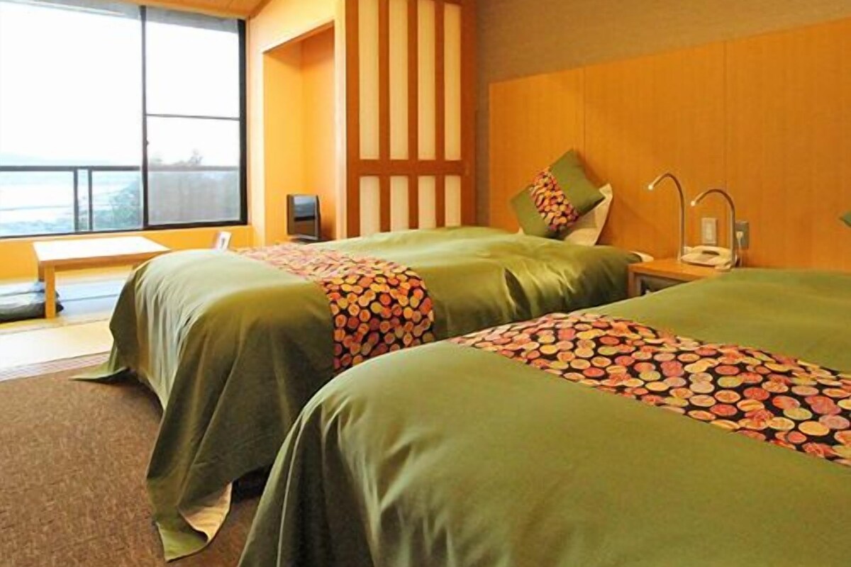 Habitación de hotel con dos camas, un banco, un ventanal grande y cabecero de madera.