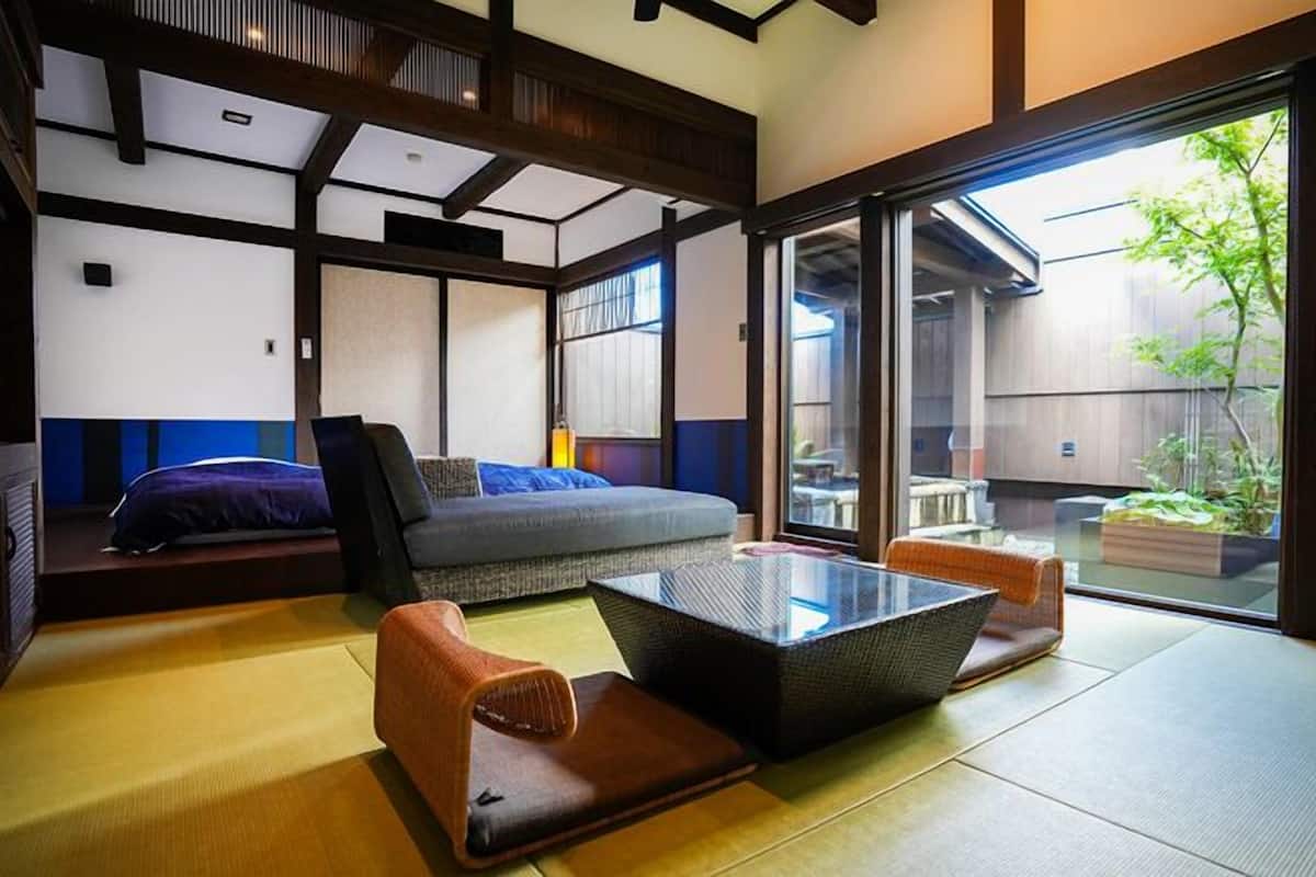 A traditional Japanese-style room with tatami flooring, a low table, cushions, and sliding doors leading to an outdoor area.