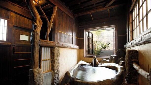 A rustic bathroom with a stone sink, wooden beams, and a window with a view. - Yunoyado Irifune (Aso)
