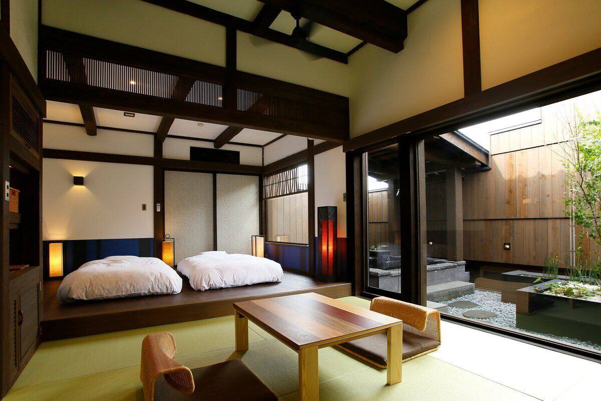 A traditional Japanese room with tatami flooring, a low wooden table, two beds with white bedding, and sliding doors leading to a garden.