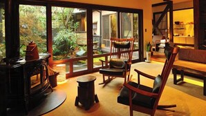 A cozy interior with a fireplace, wooden furniture, and large windows overlooking a garden. - Yunoyado Irifune (Aso)